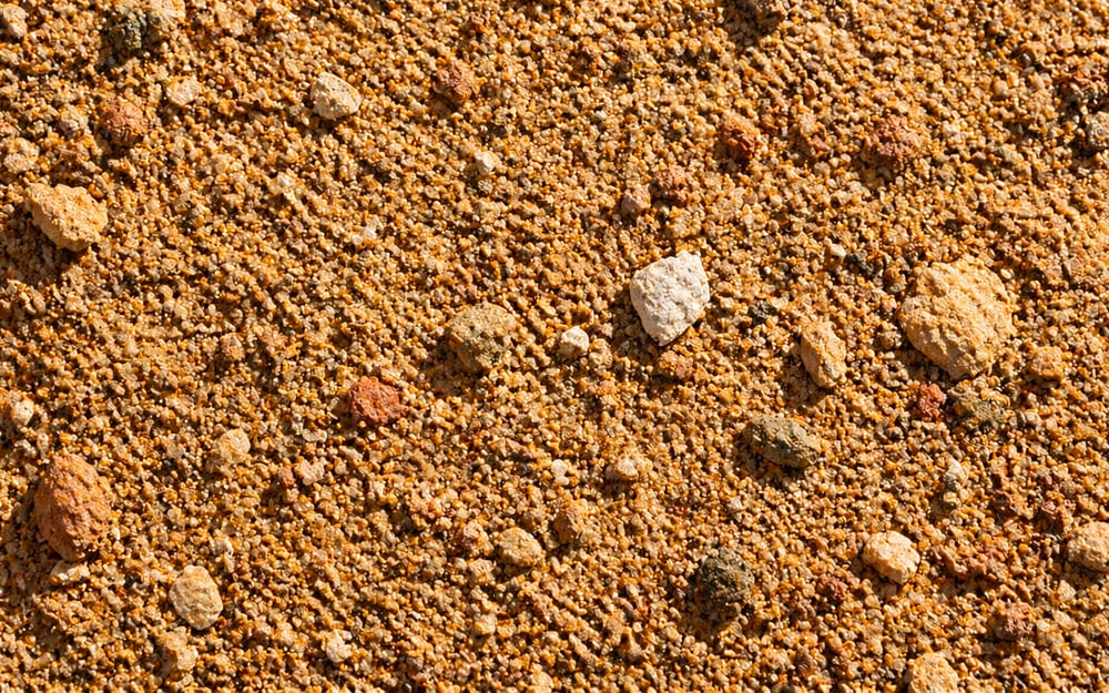 Close-up da textura de areia grossa, com pedregulhos misturados